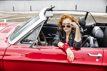 Porträt einer rothaarigen Frau mit Sonnenbrille in einem Sportwagen - FMKF04495