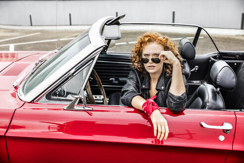 Portrait of redheaded woman wearing sunglasses in sports car - FMKF04495