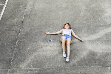 Young woman lying on parking level next to cell phone - FMKF04515