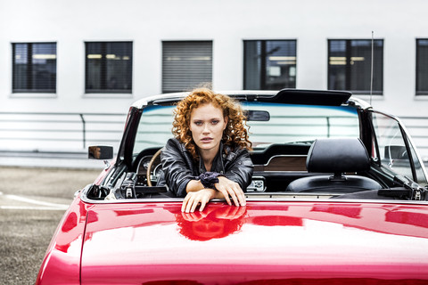 Porträt einer selbstbewussten rothaarigen Frau in einem Sportwagen, lizenzfreies Stockfoto