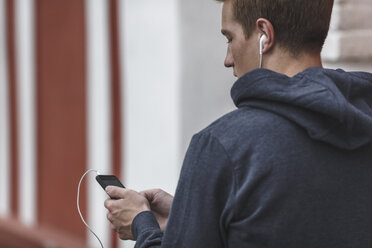 Junger Mann mit Mobiltelefon und Kopfhörern - VPIF00080