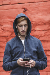 Junger Mann mit Handy und Kopfhörern an roter Backsteinmauer - VPIF00082