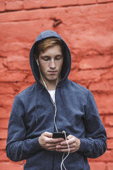 Young man with cell phone and earphones at red brick wall - VPIF00082