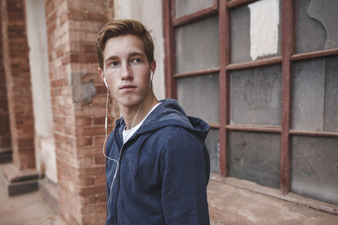 Junger Mann mit Kopfhörern an einem Backsteingebäude, der sich umschaut, lizenzfreies Stockfoto