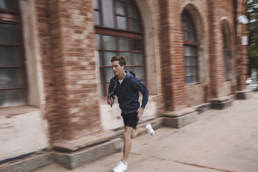 Junger Mann läuft entlang eines Backsteingebäudes - VPIF00088