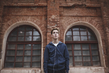 Young man with earphones standing at brick building - VPIF00093