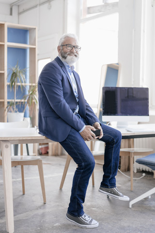 Lächelnder reifer Mann mit Bart und Brille sitzt am Schreibtisch, lizenzfreies Stockfoto