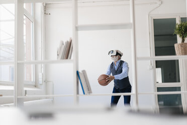 Mature man wearing VR glasses playing basketball in office - JOSF01722