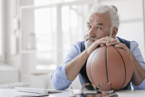 Porträt eines reifen Mannes an einem Schreibtisch mit Basketball - JOSF01726