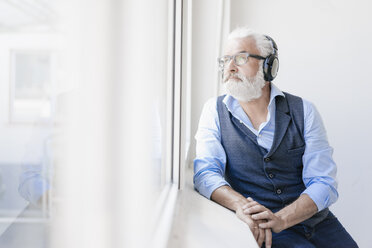 Mature man wearing glasses and headphones looking out of window - JOSF01727