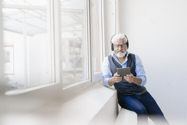 Mature man with tablet and headphones at the window - JOSF01728