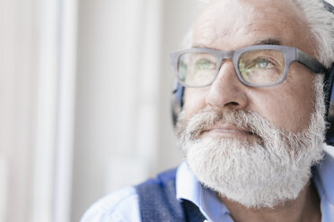 Mature man wearing glasses and headphones at the window - JOSF01730