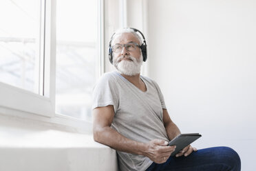 Älterer Mann mit Tablet und Kopfhörern schaut aus dem Fenster - JOSF01731