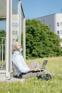 Älterer Mann mit Laptop entspannt auf einer Wiese - JOSF01734
