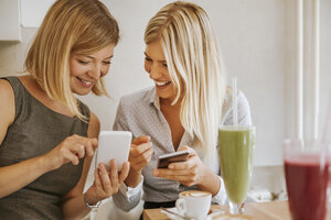 Zwei glückliche junge Frauen mit Smartphones in einem Cafe - ZEDF00862