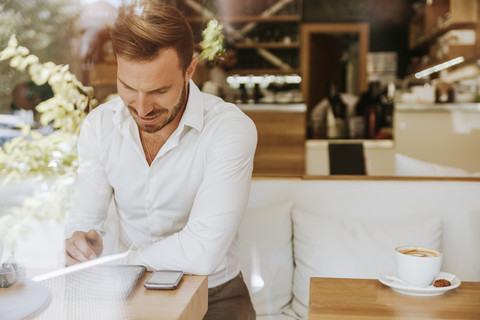 Lächelnder Mann mit Tablet und Mobiltelefon in einem Cafe, lizenzfreies Stockfoto