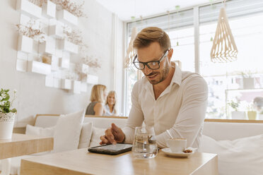 Man using tablet in a cafe with two women in background - ZEDF00865