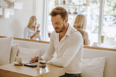 Man using tablet in a cafe with two women in background - ZEDF00866