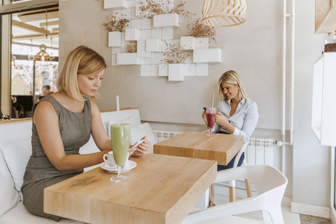 Zwei junge Frauen benutzen Smartphones in einem Café, lizenzfreies Stockfoto