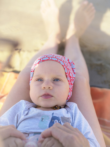 Porträt eines kleinen Mädchens, das auf den Beinen seiner Mutter am Strand liegt, lizenzfreies Stockfoto
