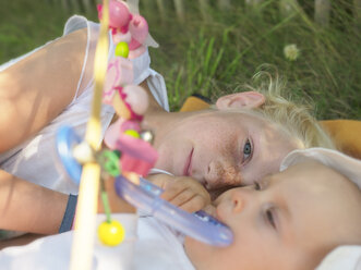 Freckled girl lying with baby girl on blanket on a meadow - LAF01887