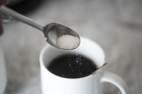 Sugar on coffee spoon in front of mug with black coffee - CHPF00430
