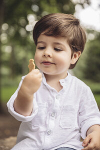 Porträt eines Kleinkindes mit Blick auf einen Keks im Park - MFF03961