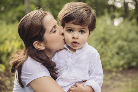 Mother kissing toddler on cheek in park stock photo