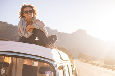 Spain, Tenerife, portrait of happy woman sitting on car roof of van at twilight - SIPF01755