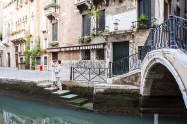 Italien, Venedig, Brautpaar steht sich auf einer Treppe in der Nähe eines Kanals gegenüber - DIGF02849