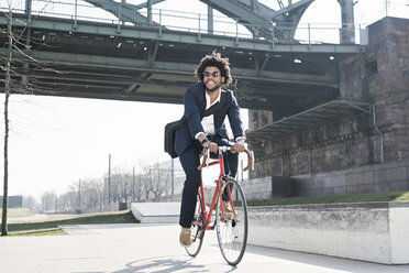 Lächelnder Geschäftsmann auf dem Fahrrad an einer Brücke am Flussufer - SBOF00675