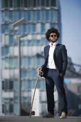 Businessman with longboard standing in front of skyscraper - SBOF00684