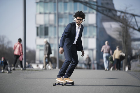 Geschäftsmann fährt Longboard vor einem Wolkenkratzer, lizenzfreies Stockfoto