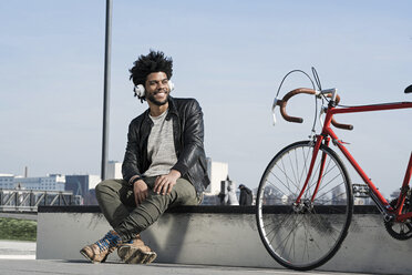 Lächelnder Mann, der neben seinem Fahrrad über Kopfhörer Musik hört - SBOF00690