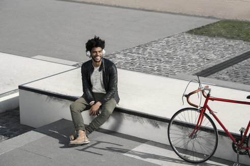Lächelnder Mann, der neben seinem Fahrrad über Kopfhörer Musik hört - SBOF00691