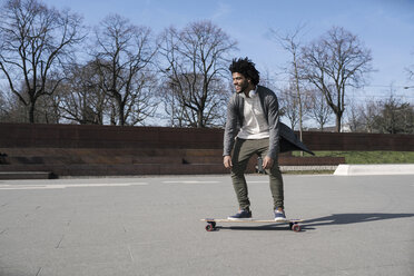 Lächelnder junger Mann fährt Longboard im Skatepark - SBOF00693