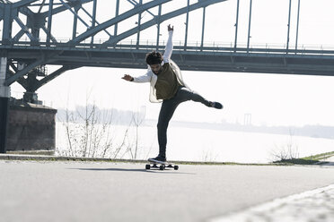 Young man balancing on longboard at the riverside - SBOF00697