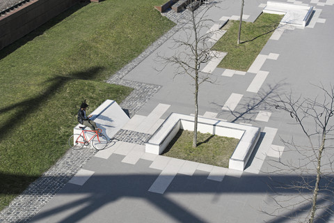 Man sitting in city skatepark with smartphone next to his bicycle stock photo