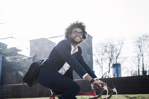 Lächelnder Geschäftsmann mit Sonnenbrille auf dem Fahrrad in der Stadt, lizenzfreies Stockfoto