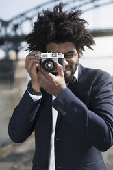 Man in suit at the riverside taking a picture with a vintage camera - SBOF00726