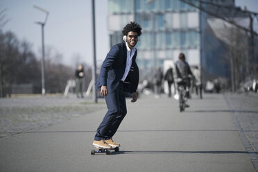 Smiling businessman riding longboard in front of skyscraper - SBOF00730