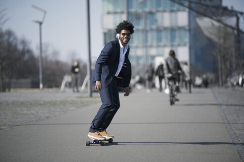 Lächelnder Geschäftsmann auf Longboard vor einem Wolkenkratzer - SBOF00730