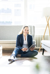 Smiling businesswoman sitting on floor using tablet - JOSF01746