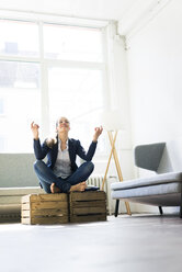 Businesswoman sitting on crate practising yoga - JOSF01754