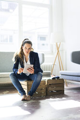 Businesswoman sitting on a crate using tablet - JOSF01757