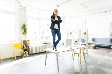 Porträt einer Geschäftsfrau, die auf einem Tisch in einem Loft steht - JOSF01762