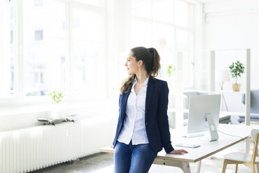 Businesswoman leaning on desk looking out of window - JOSF01769