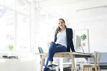 Portrait of smiling businesswoman sitting on table in a loft - JOSF01773