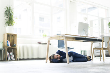 Geschäftsfrau liegt unter dem Tisch im Büro und schläft - JOSF01774