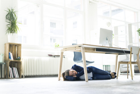 Businesswoman lying under the table in office sleeping - JOSF01774
